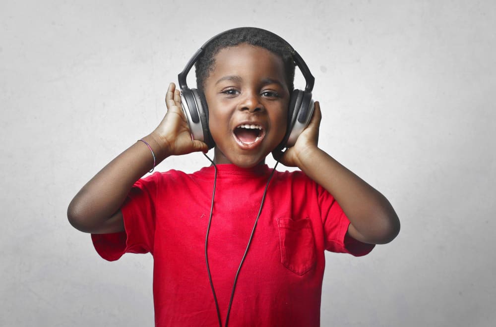 A boy in a red shirt wearing headphones, mouth wide open mid-song.