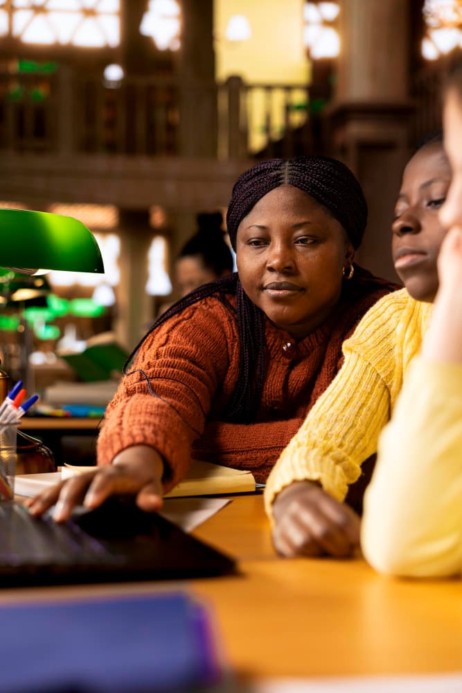 A tutor sitting alongside a young learner at a desk, working through a book together.